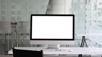 White blank screen monitor putting on white working desk with wireless mouse and keyboard over...