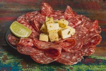 Comida de boteco brasileira linguiça calabresa fatiada fina com queijo em cubos servido em tigela em balcão de boteco