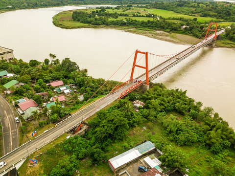 Magapit Suspension Bridge and Cagayan River, largest by volume and longest river in the Philippines.  Aerial shot of wide meandering river and red bridge.