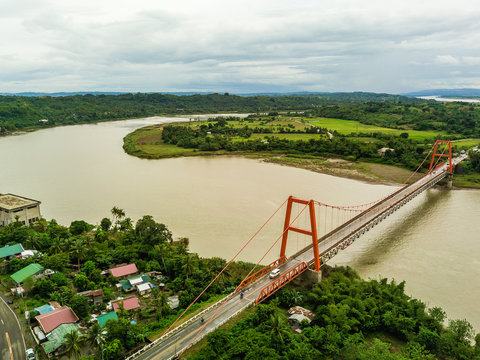 Magapit Suspension Bridge and Cagayan River, largest by volume and longest river in the Philippines.  Aerial shot of wide silty river and red bridge.