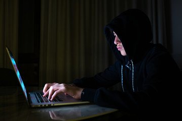 Hacker is  hacking into the computer network. Young boy in a dark room with laptop.  Hacker with a laptop.