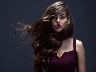 Face of a beautiful woman with long brown curly hair. Fashion model with wavy hairstyle. Attractive young  girl with curly hair posing at studio. Female face with purple makeup. Violet make-up.