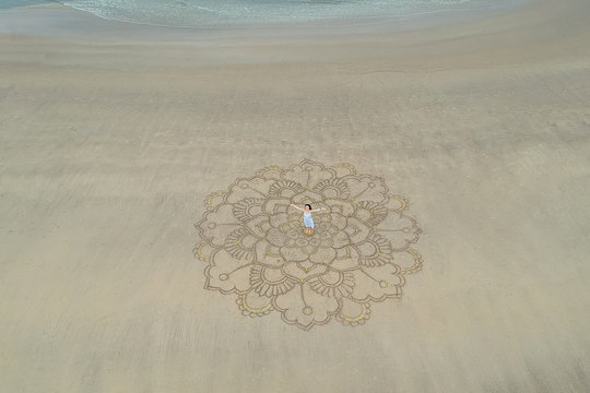 a large mandala painted on the sand on the ocean with a girl in the middle.