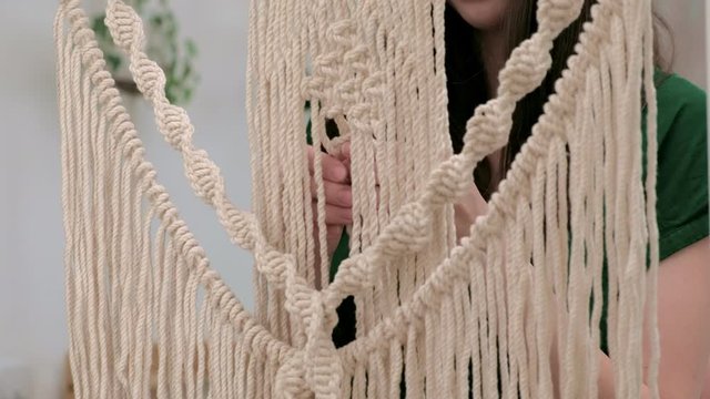 woman weaves macrame on a stick.
