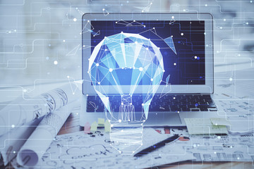 Computer on desktop in office with bulb icon hologram. Multi exposure. Concept of idea.