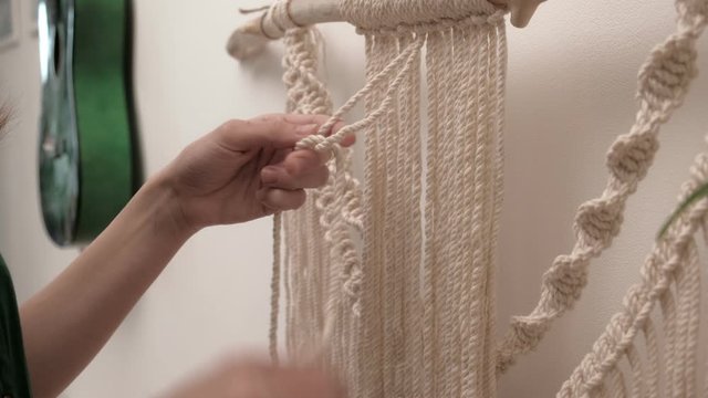 woman weaves macrame on a stick.