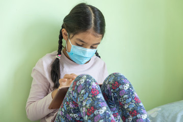 An 8 year old girl wears a mask during quarantine and spends time on her tablet.