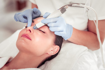 Cosmetologist using modern equipment for face cleansing