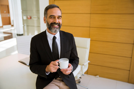Handsome middle aged businessman holding cup of coffee or in the office