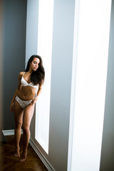 Portrait of sexy woman in lingerie standing by window in bedroom