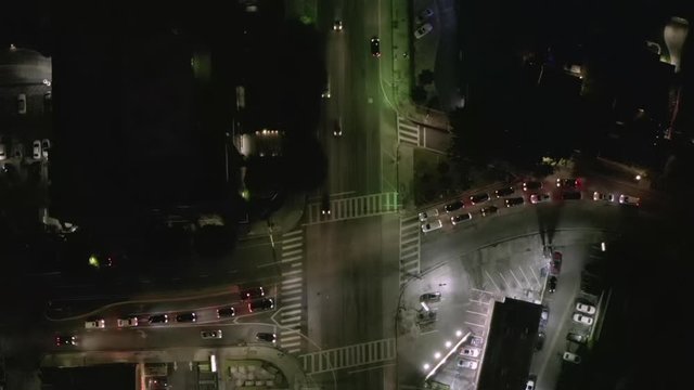 AERIAL: Overhead View of Street at Night with Store Parking Lot and City Car Traffic Lights 