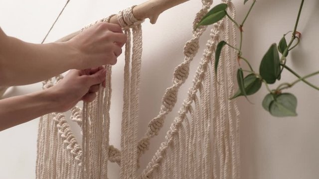 woman weaves macrame on a stick.