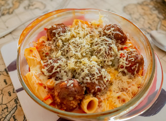  Close up and selective focus of pork and beef meatballs on a bed of pasta topped with melted grated cheddar cheese and mixed herbs