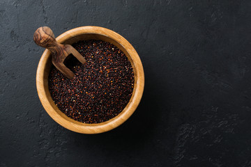 Black quinoa grains seeds in a bamboo bowl on a black stone background. Flat lay with copy space.