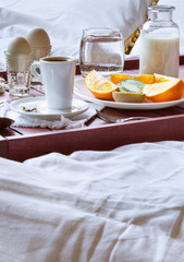 Fototapeta na wymiar Breakfast in bed on wooden tray with fruits, milk, eggs and coffe. Window light, copy space