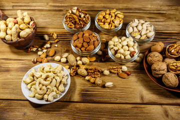 Assortment of nuts on wooden table. Almond, hazelnut, pistachio, peanut, walnut and cashew in small bowls. Healthy eating concept