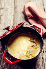 Creamy Polenta with baked onion and cheese in cast iron pot on rustic wooden background. Italian food. Selective focus. Toned image