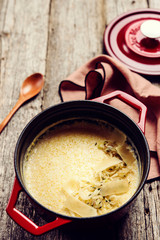 Creamy Polenta with baked onion and cheese in cast iron pot on rustic wooden background. Italian food. Selective focus. Toned image