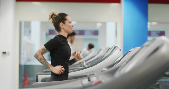 Young woman running on a treadmill at gym. Side view. Woman training at fitness center. Woman exercising cardio workout