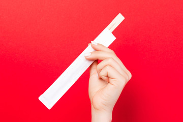 Woman's hand holding chopsticks in a pack on red background. Chinese food concept with empty space for your design