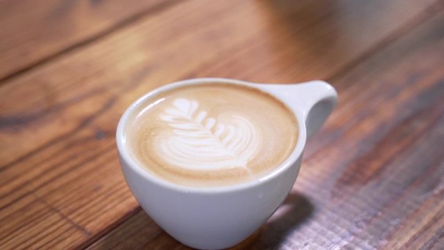 Man serves hot cappuccino with latte art. Male places coffee mug on a wooden table at a cafe coffee shop. Slow motion stock footage.