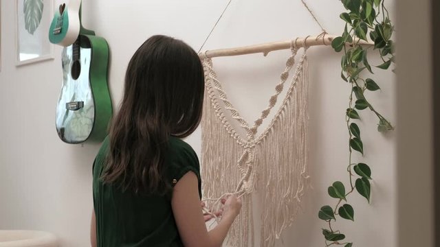 woman weaves macrame on a stick.