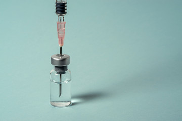 Long syringe needle pierces the cap of medical vial with transparent liquid. Close-up on blue background.