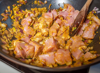 Close up of cubed pork loin, chopped garlic, chopped red onion and a variety of spices frying off...