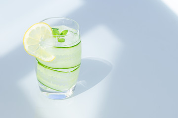 Glass of water with lemon, ice, and cucumber isolated on a blue background, copy space.