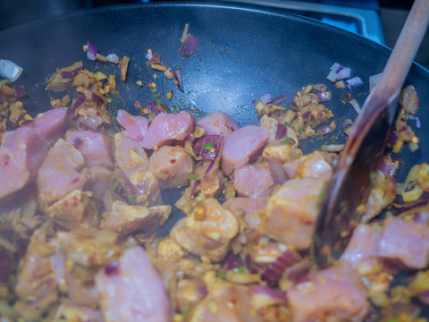  Close Up Of Steaming And Sizzling Cubed Pork Loin, Sliced Garlic, Chopped Red Onions And Various Spices Frying In A Non-stick Pan On The Hob Whilst Making A Hot And Spicy Pork Madras Curry Dinner