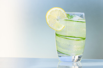 Glass of water with lemon, ice, and cucumber isolated on a blue background, copy space.