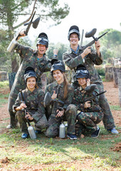 Team of excited friends paintball players in camouflage standing with guns