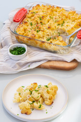 Macaroni and cheese in transparent dish on cotton towel on the table. There is a spoon inside it. One portion in the plate. Homemade vegetarian lunch or dinner. Close up. 