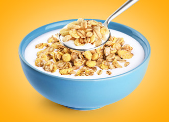 Bowl and spoon with oat granola, milk, yogurt on orange background.