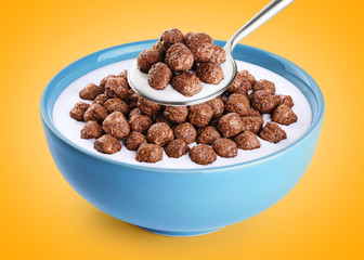 Bowl and spoon with chocolate corn balls, milk, yogurt on orange background.