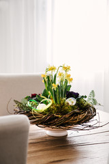 Easter table centerpiece decoration with daffodils and easter eggs arranged in a rustic wreath made with tree twigs.