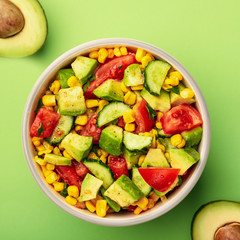 Top view tasty avocado salad with tomatoes, cucumbers in bowl on green background