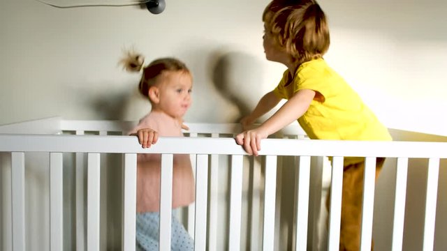Side view of little boy and girl in pajamas screaming and jumping in crib while playing at home together