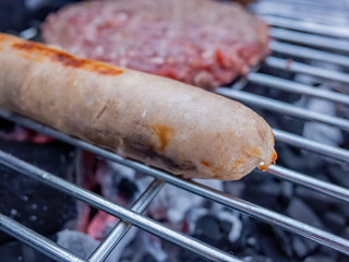 Pork sausage and beef burger on a charcoal BBQ with close up and selective focus on the pork sausage