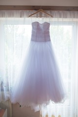 Wedding dress with crystals and pearls hangs
Elegant wedding dress with a train hanging on window....
