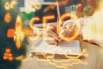 Multi exposure of woman's hands making notes with SEO icon. Concept of Search engine optimization