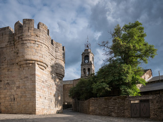 View of the church tower and the castle of Puebla de Sanabria, a robinia tree and dramatic clouds at sunset