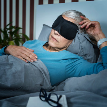 Mature Woman Wearing Black Sleep Mask, Lying In Bed