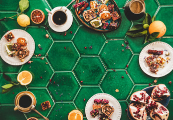 Flat-lay of variety of Turkish traditional lokum sweet delight with Turkish coffee in cups over green Moroccan tile table, top view, copy space. Middle East typical dessert food