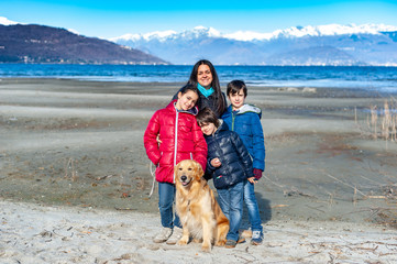 family portrait mother with three children and a golden retriever dog posing on the beach in winter