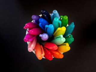 Top down view of colouring pens spiralling in a pot against a black background