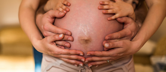 Parents hands making a heart on the belly of the pregnant mother. Mom and Dad with hands on the baby.