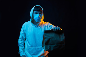 delivery man in white clothes in medicine mask with a yellow backpack on a black background