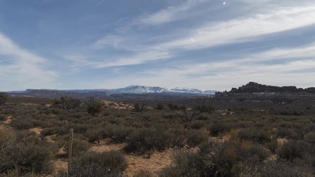 A wide timelapse of Arches National Park looking towards the distant La Sal Mountains and the Windows Section of the park. Clouds flow overhead.