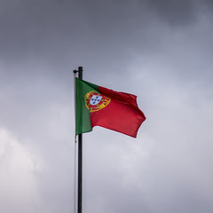 Portuguese flag flying in the wind in front of a background of dark, threating clouds